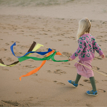 Child walking on beach holding colourful flag wearing pink and green wool cardigan.