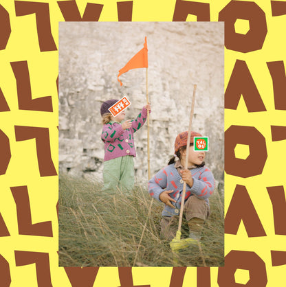  Children in wool knitwear holding flags on sand dunes.