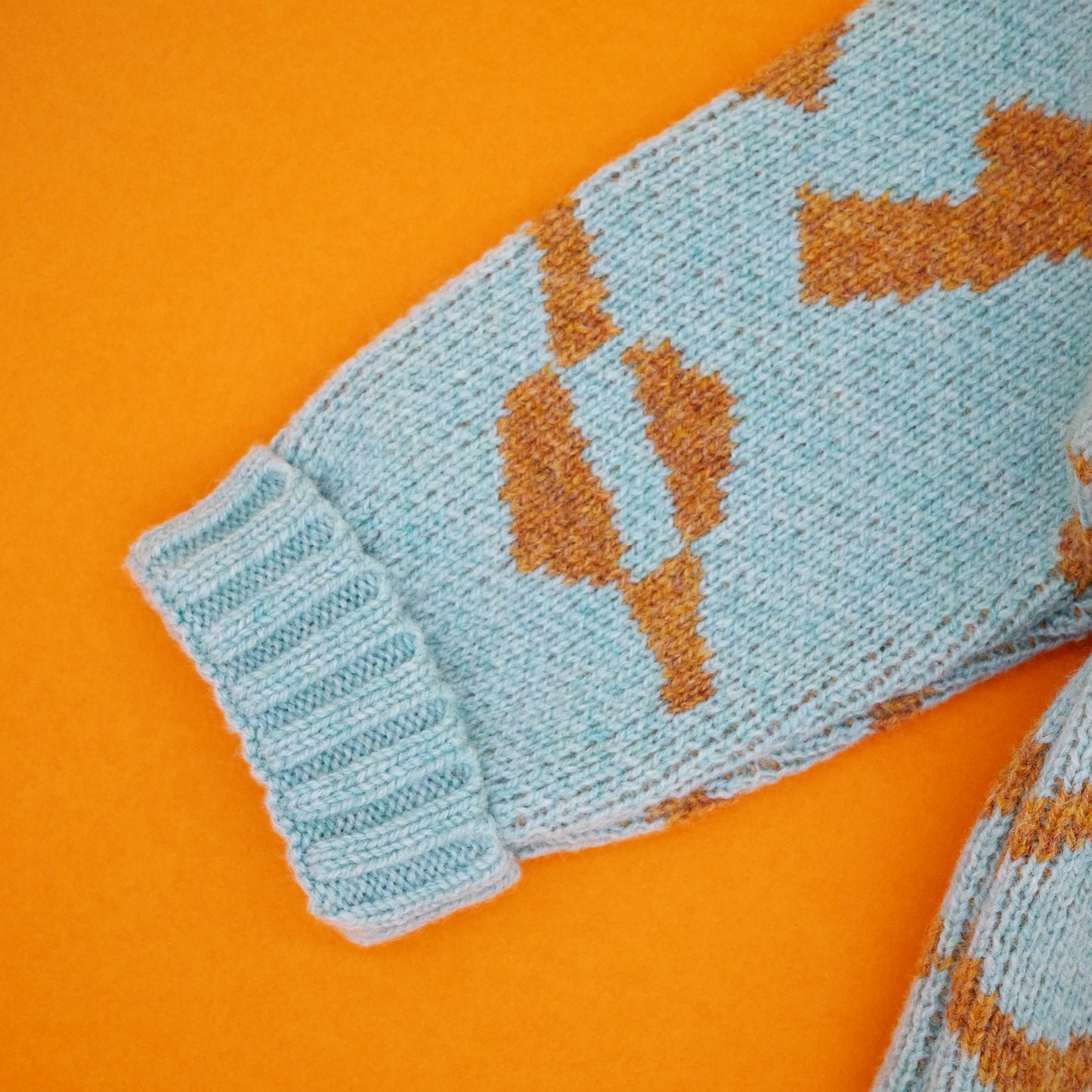 Fold back cuff of children's wool cardigan in mint and orange jacquard.